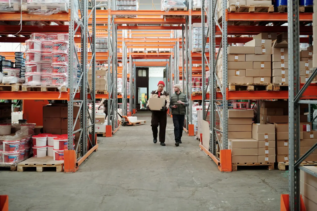 Two warehouse workers walking down an aisle of stocked shelving